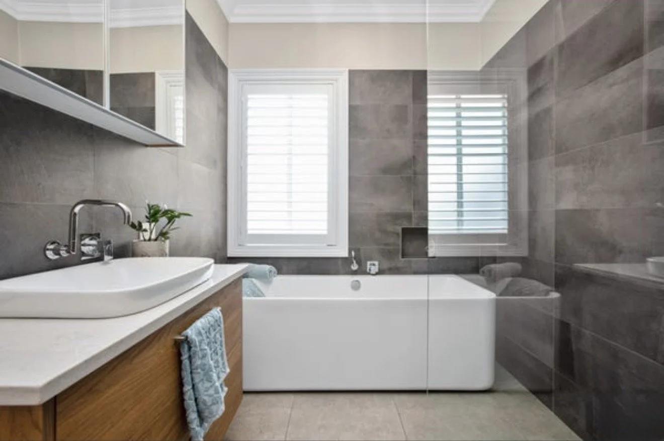 Modern bathroom with gray tiled walls, a white freestanding bathtub