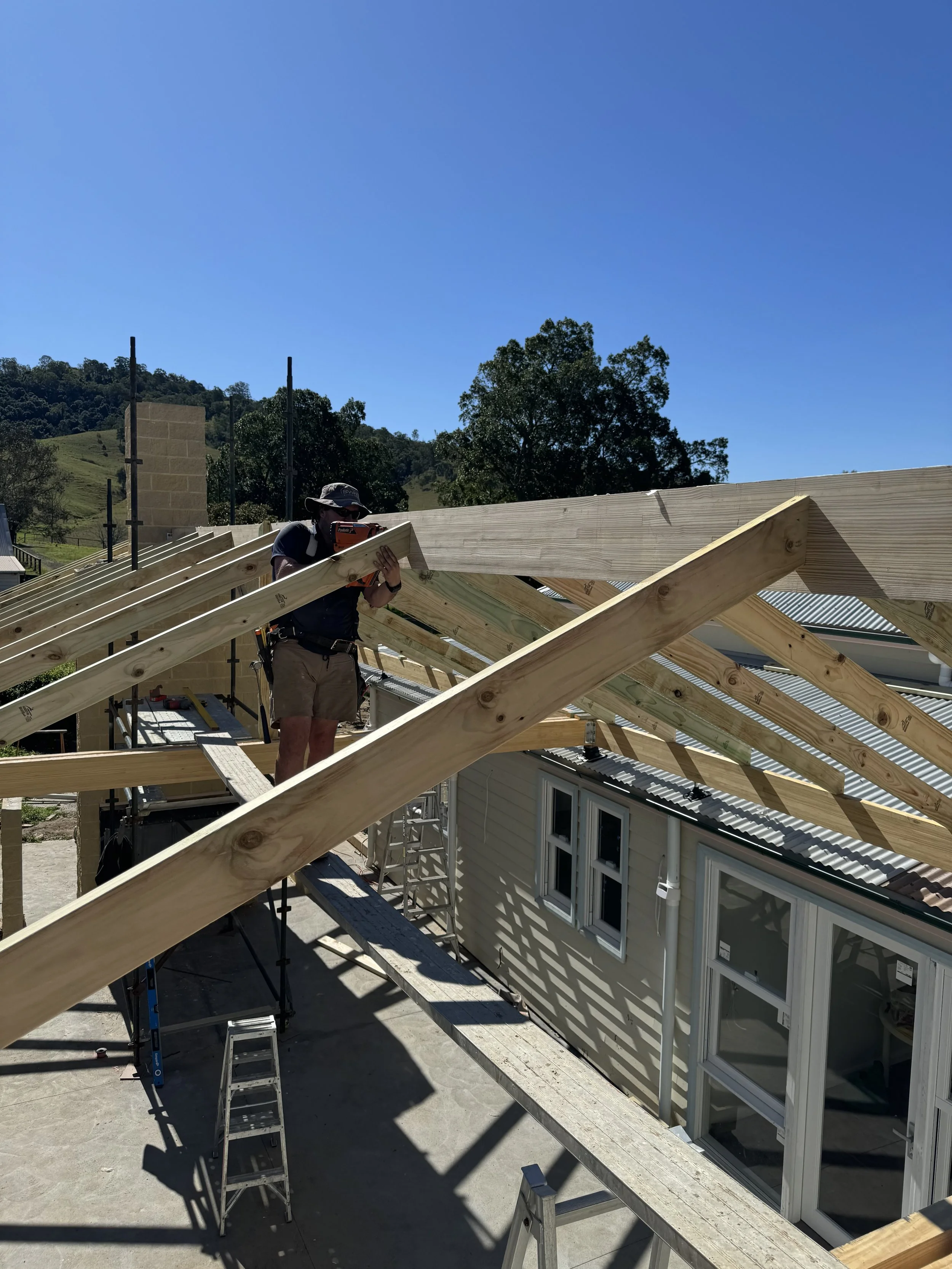 A person building a roof with wooden beams on a house in a rural area