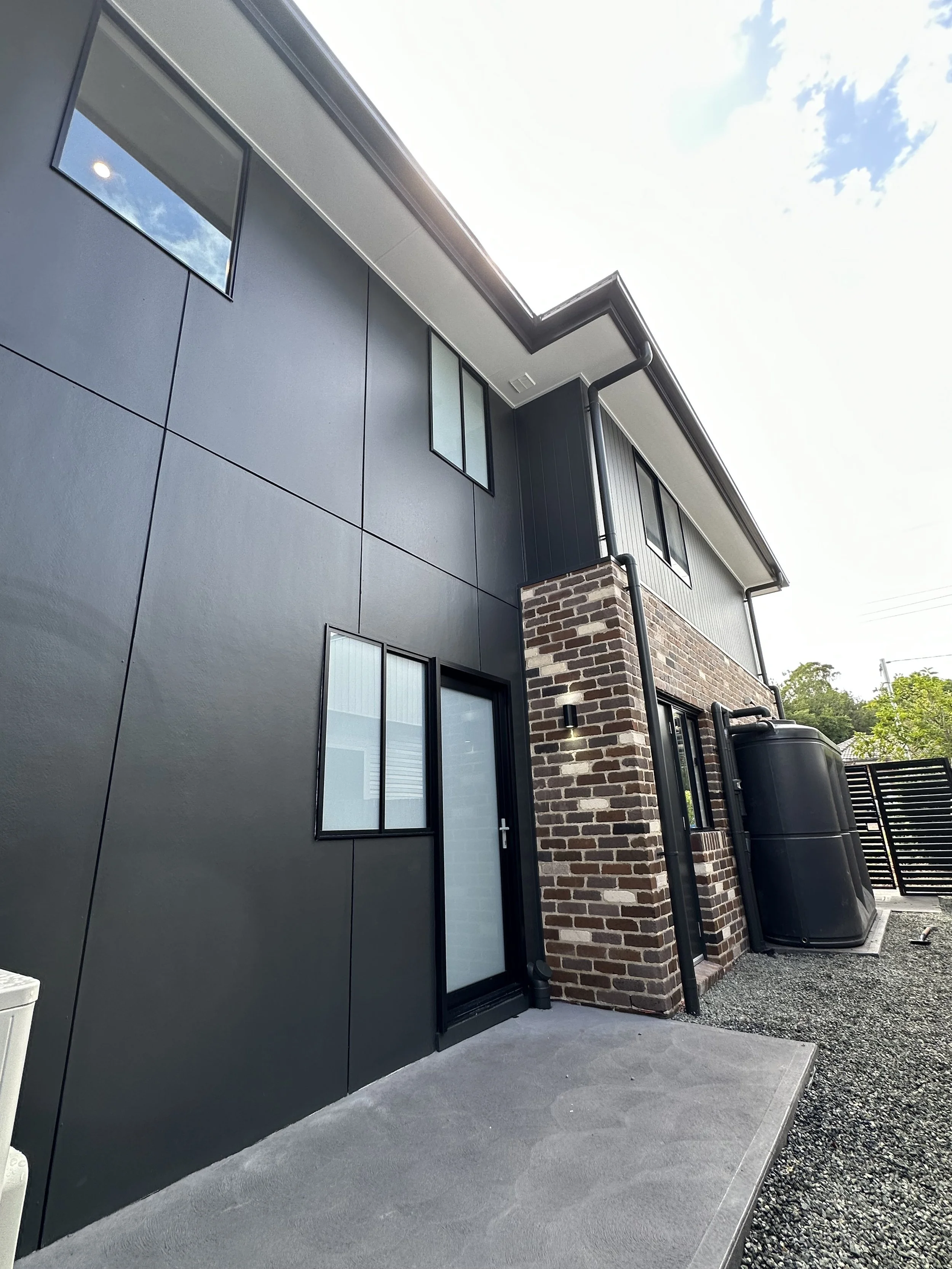 Modern residential building with black exterior walls, brick accents, and several windows 