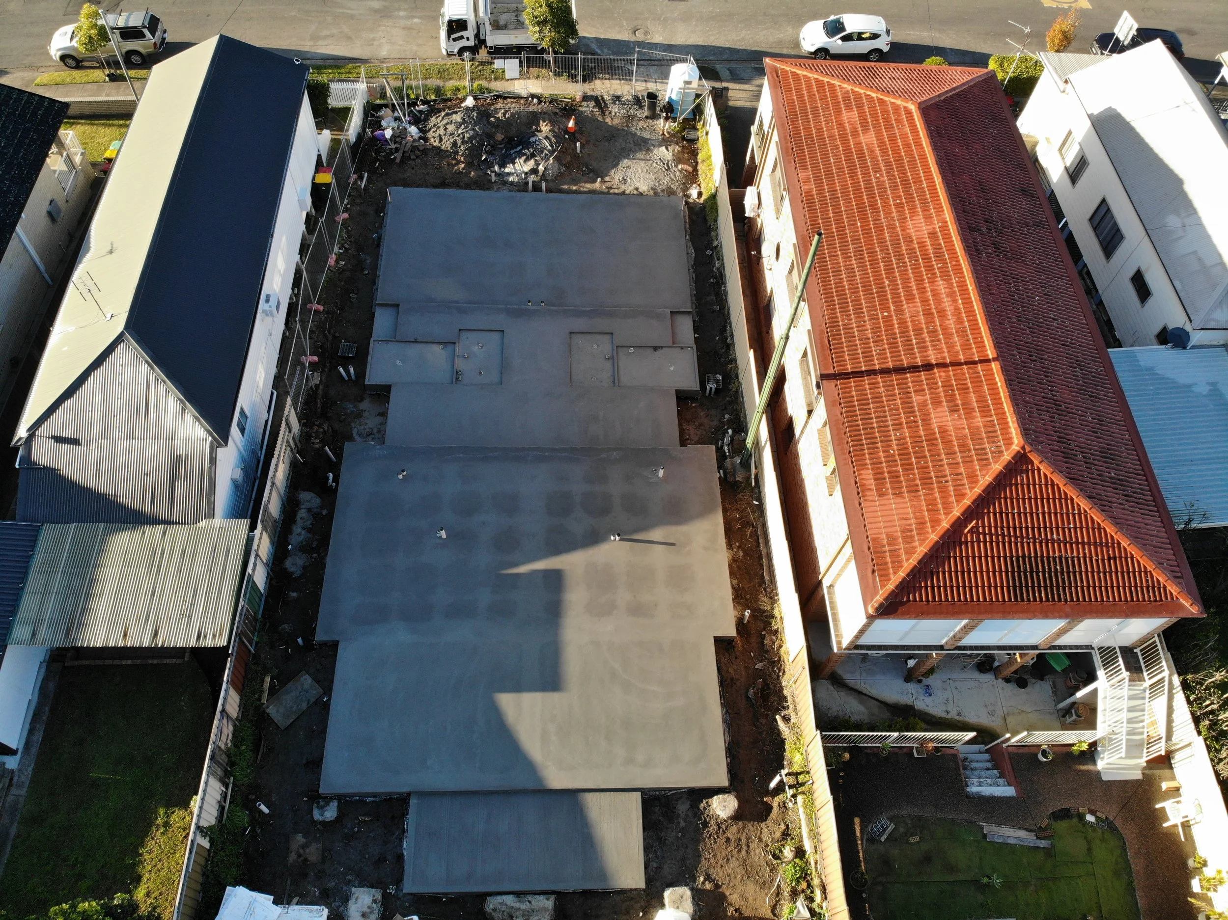 An aerial view of a residential construction site where a new building is being built. The site includes a concrete foundation, construction materials, and equipment. 