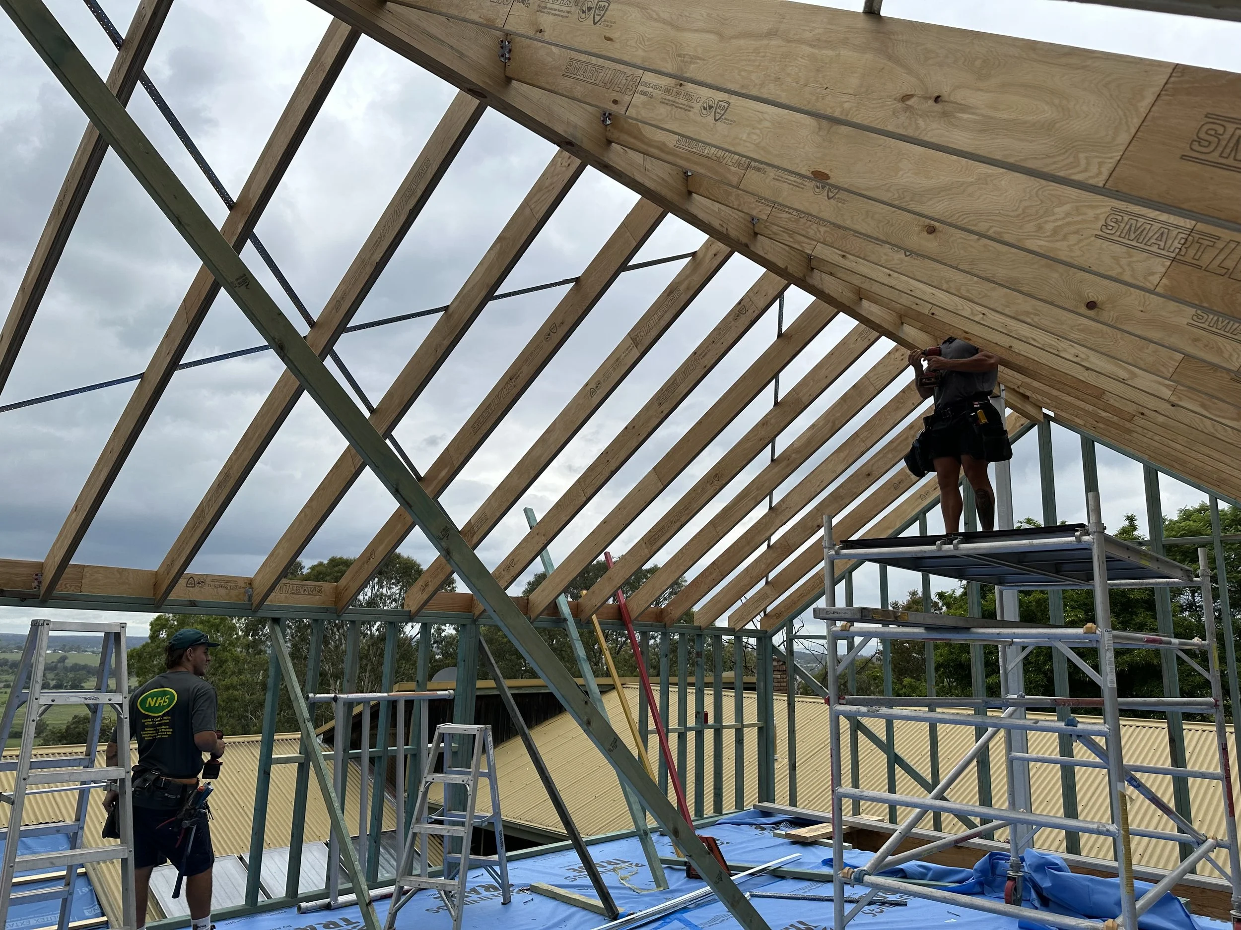 Construction workers building a wooden roof structure with exposed trusses. 