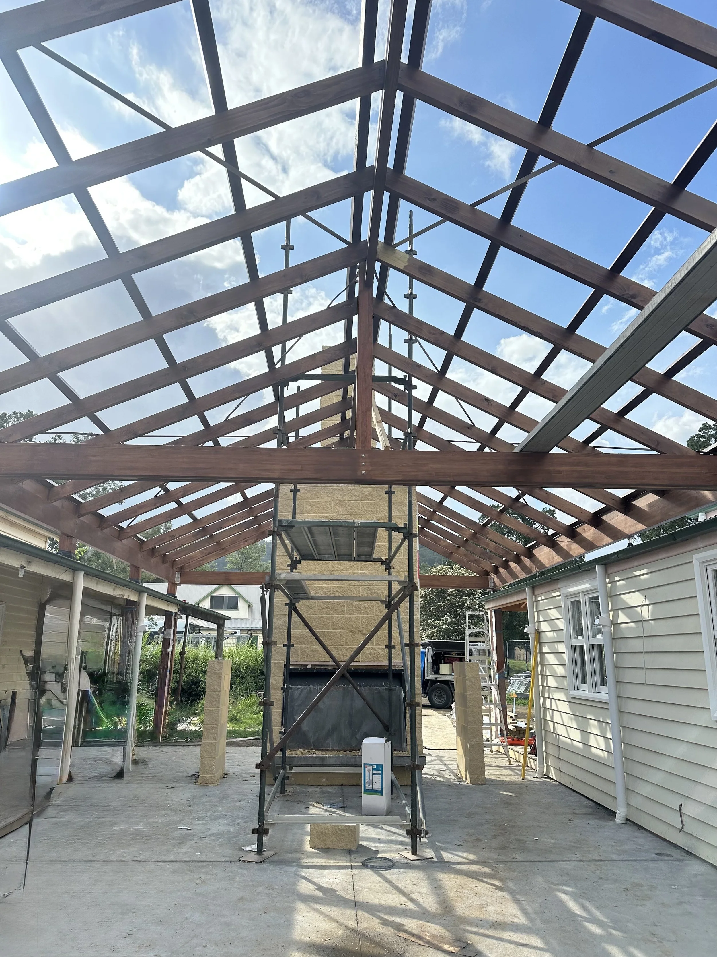 Construction site with wooden roof frame on a house, scaffolding in the middle, and other building materials around.