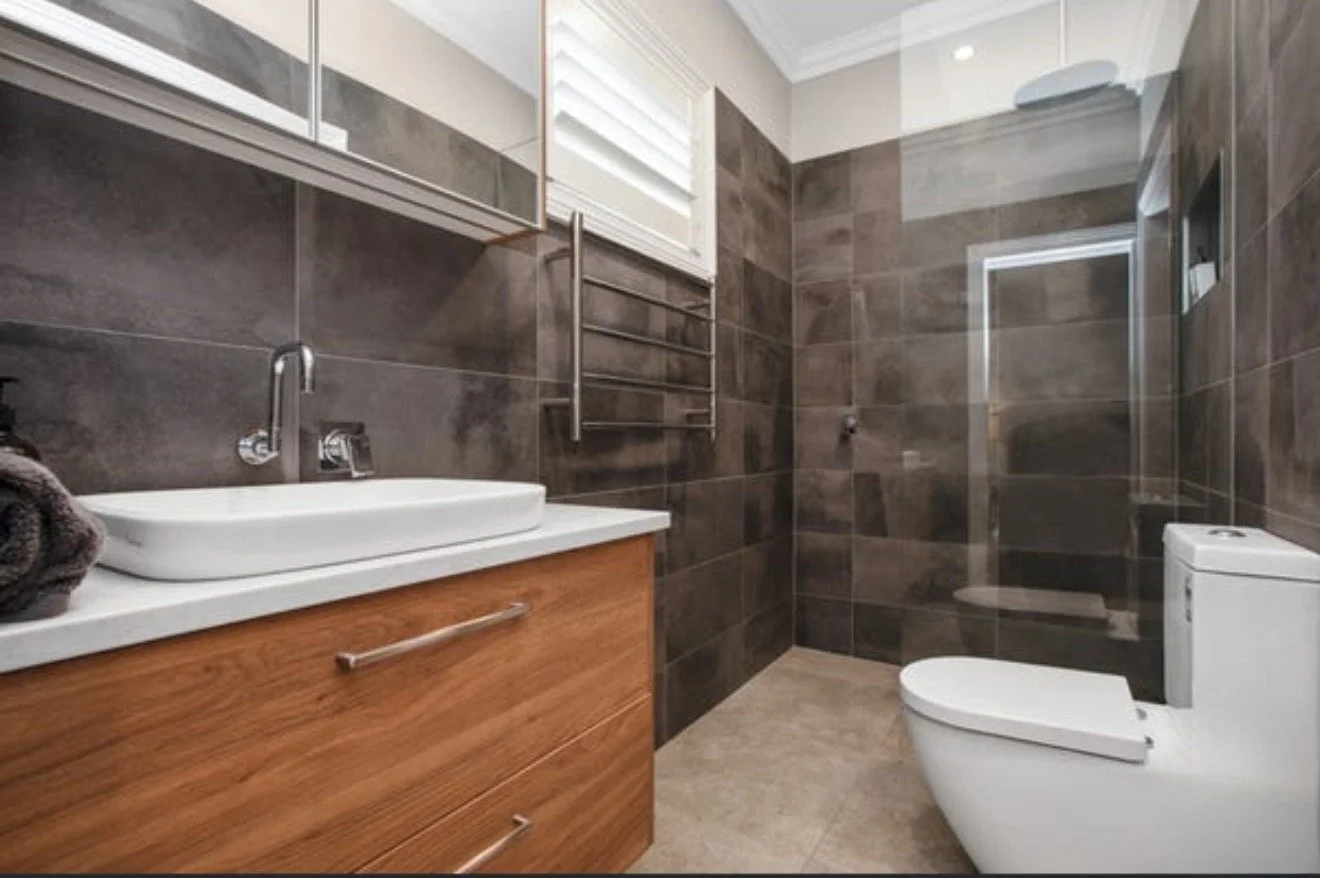 Modern bathroom featuring a wooden vanity with a white vessel sink, a wall-mounted faucet