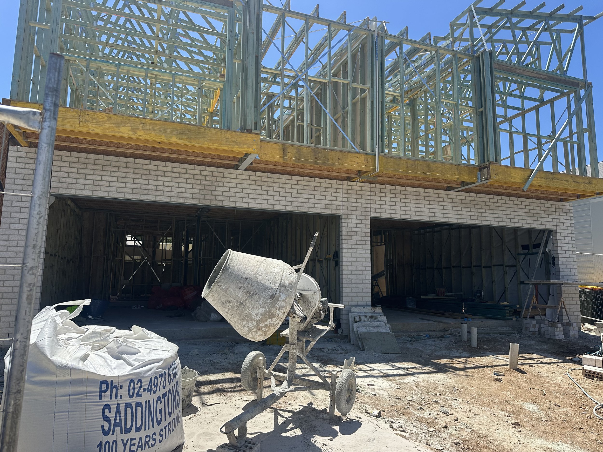 Construction site with framing for a building, a cement mixer, construction materials, and a scaffolding structure