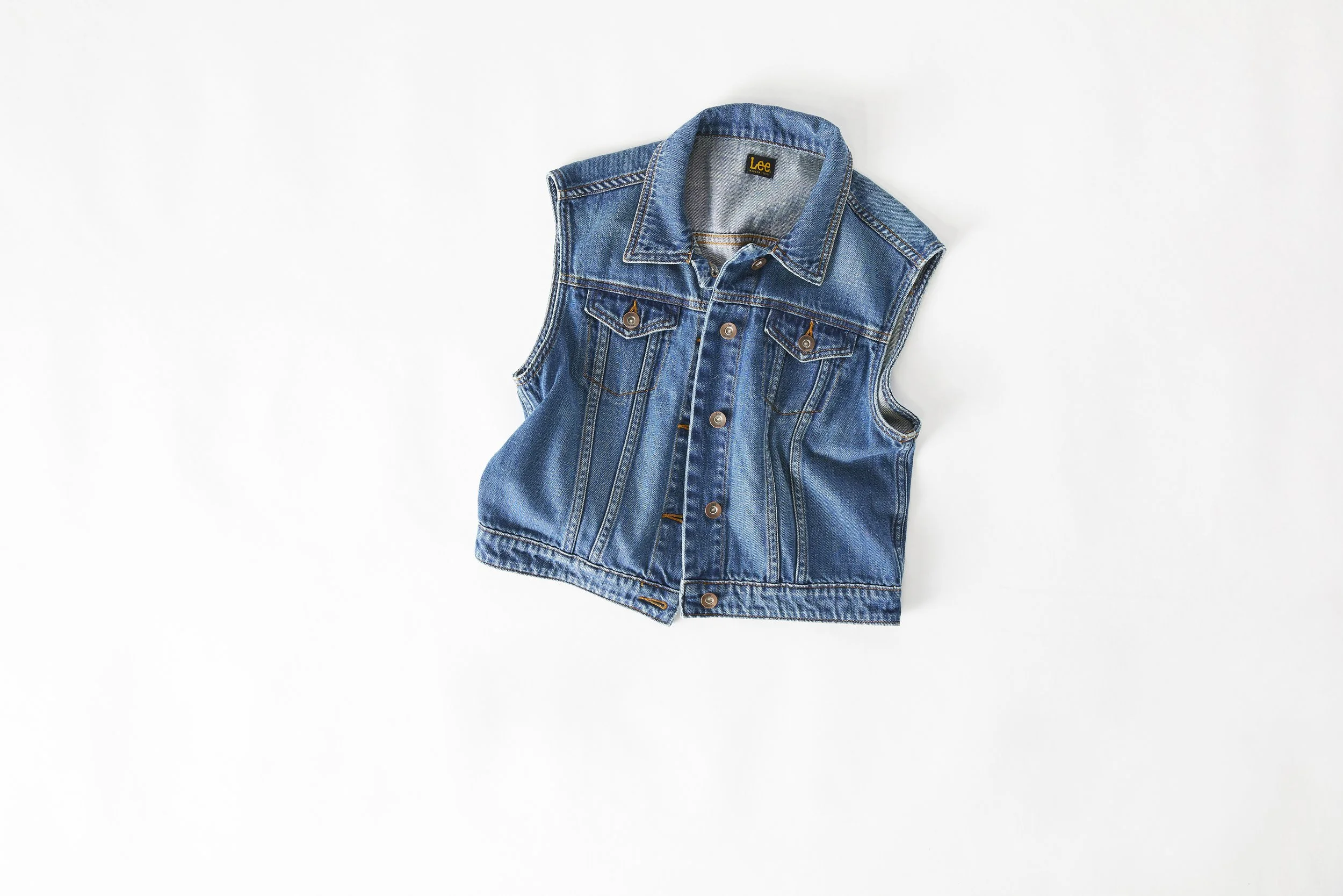 A sleeveless denim vest with button closures laid flat on a white background.