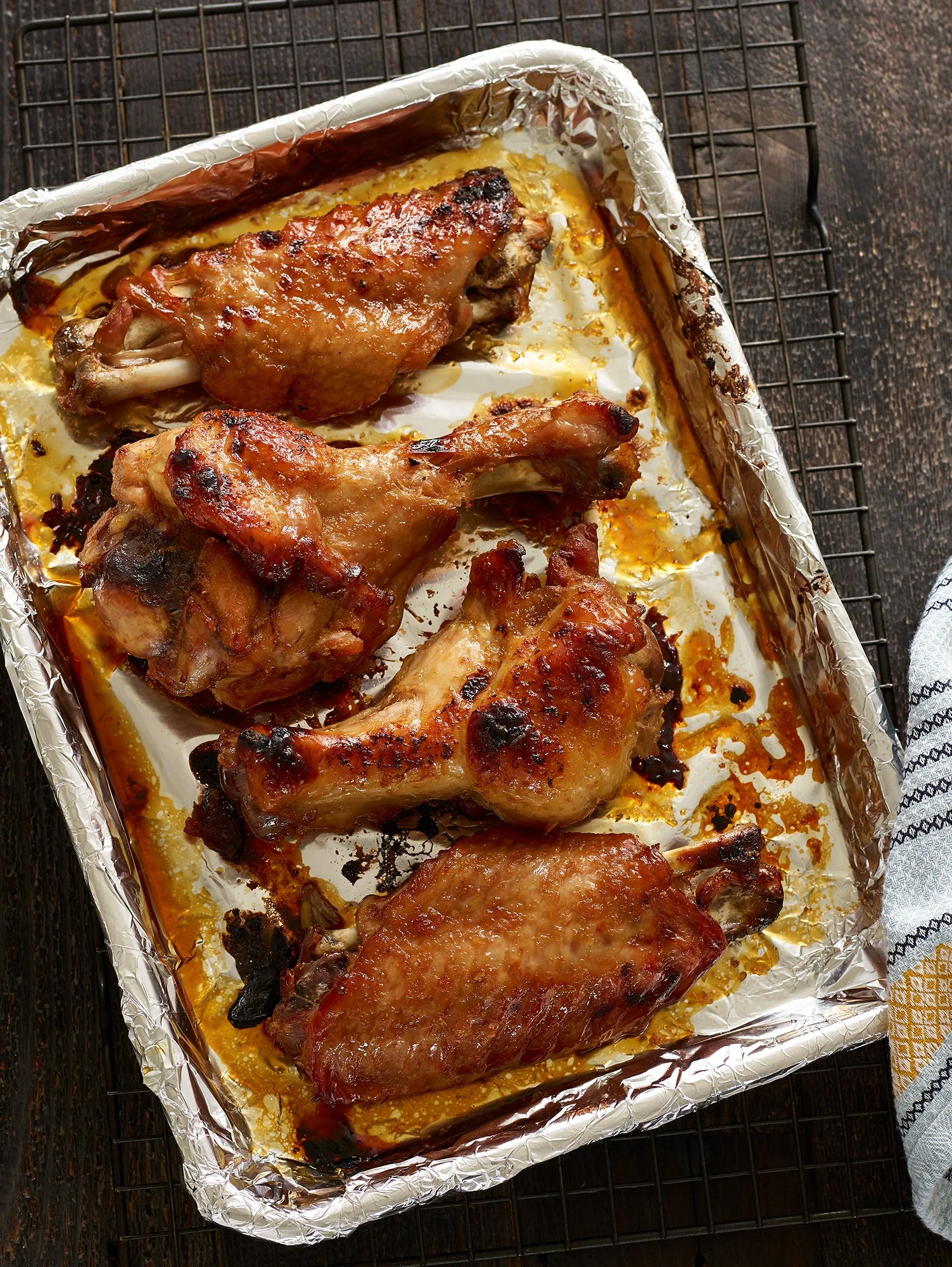 Baked chicken drumsticks and thighs on a baking sheet lined with aluminum foil, resting on a cooling rack, with some charred areas.