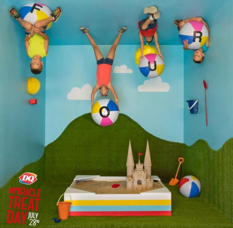 Children playing with beach balls in a sandbox indoor play area with a castle and colorful decorations, celebrating Dairy Queen's Miracle Treat Day on July 28th.