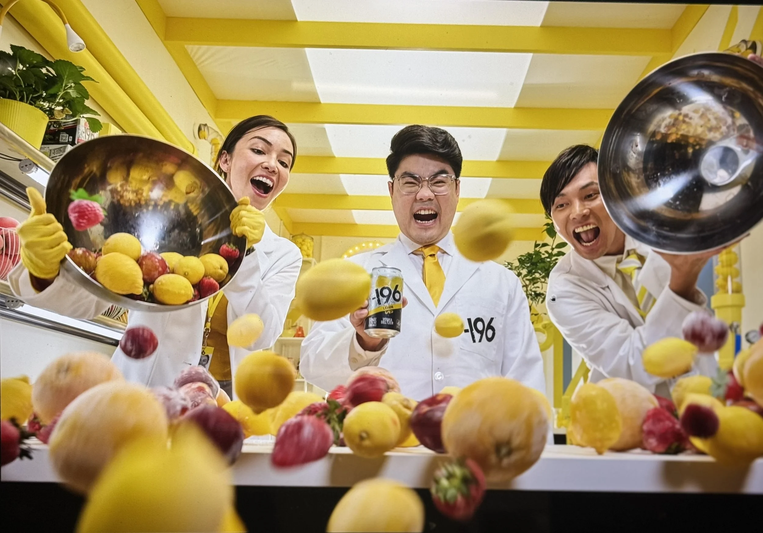 Four people in white clothing and yellow gloves tossing apples in a yellow and white room.