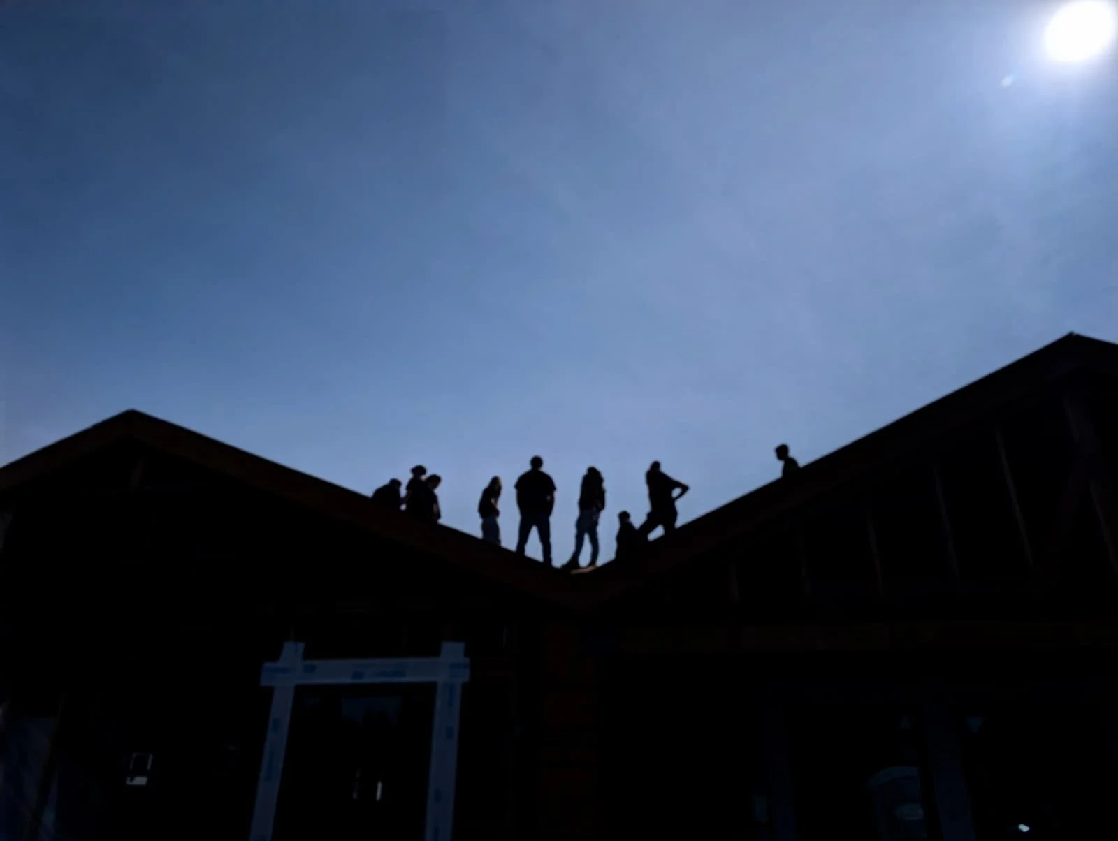 Silhouetted group of people standing on the roof of a building against a clear blue sky with the sun shining.