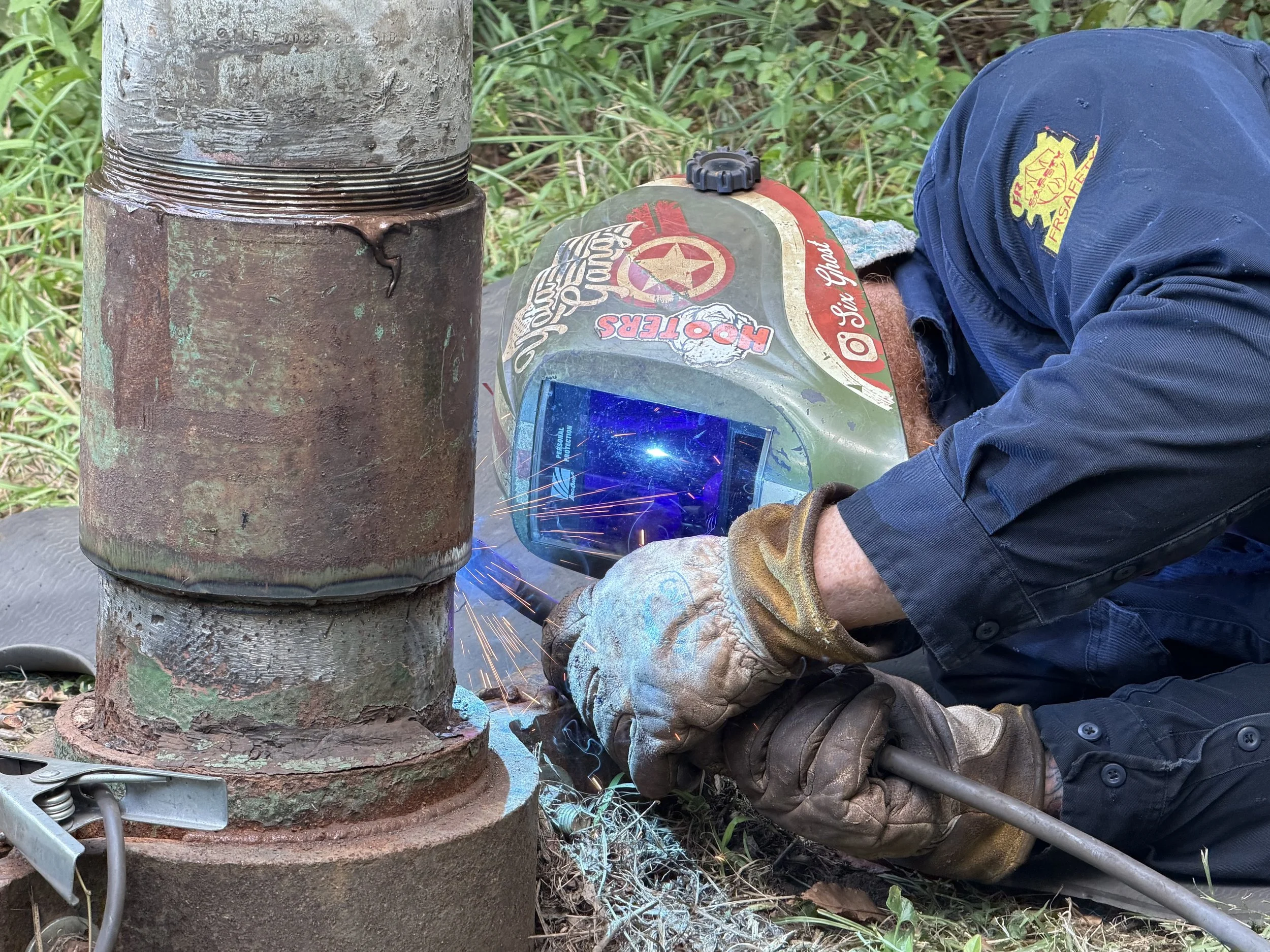A person welding on a  metal pipe creating bright sparks and blue smoke.
