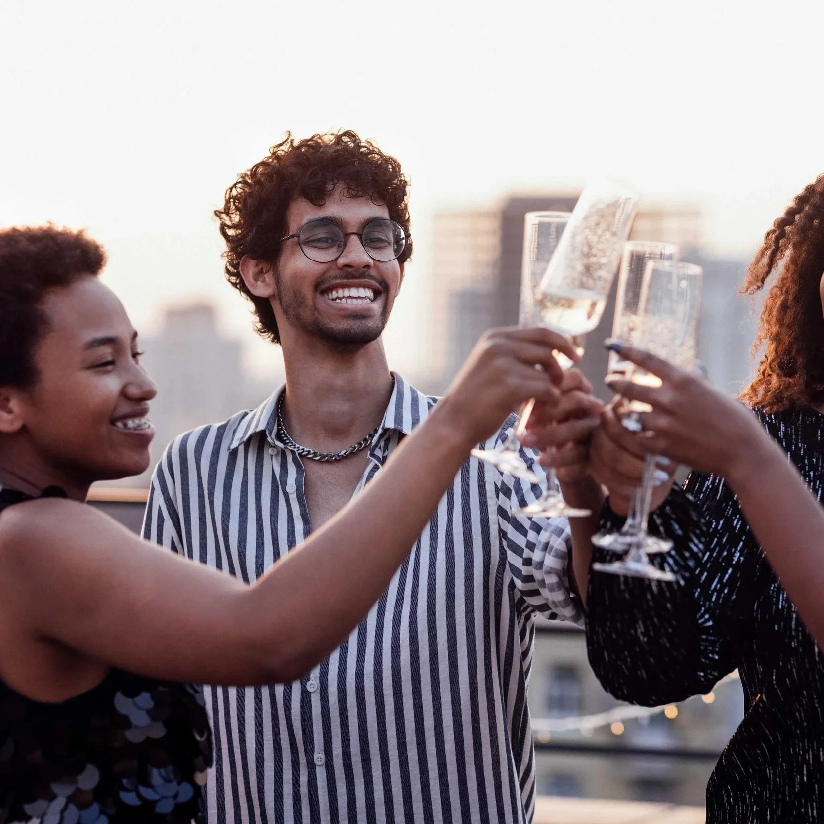Group of friends celebrating with champagne toasts outdoors in the evening, smiling, with city buildings in the background.