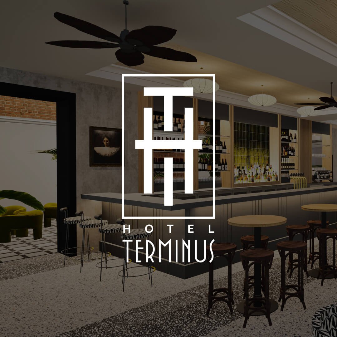 Interior of Hotel Terminus with a seating area, bar counter, and shelves stocked with bottles, with the Hotel Terminus logo overlayed