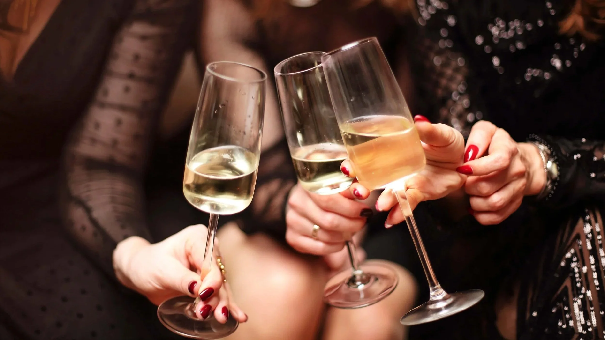 Three women clinking glasses of white wine at a celebration.