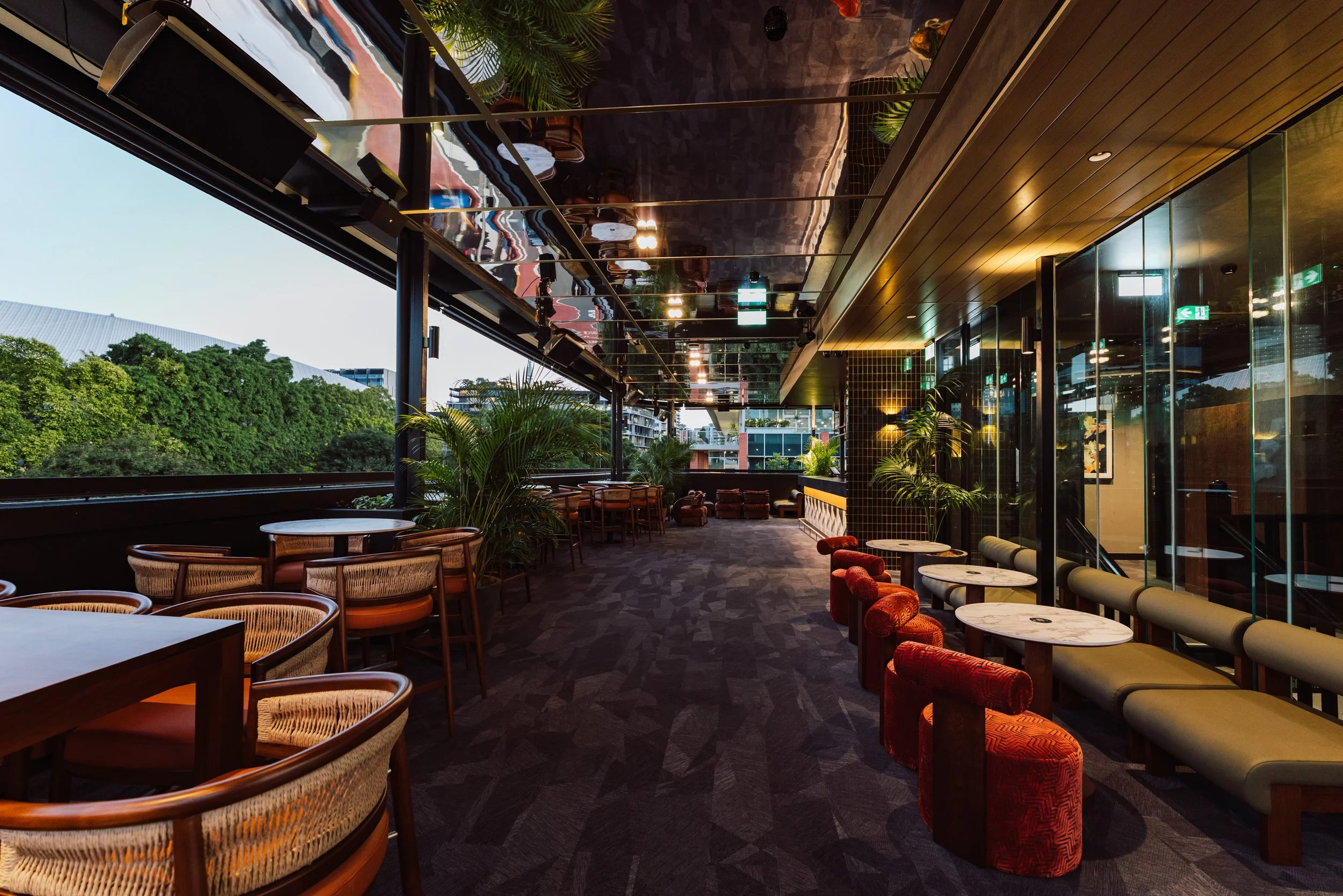 Modern dining area with wooden table, white chairs, tall plants in black pots, decorative lamps, and patterned flooring.
