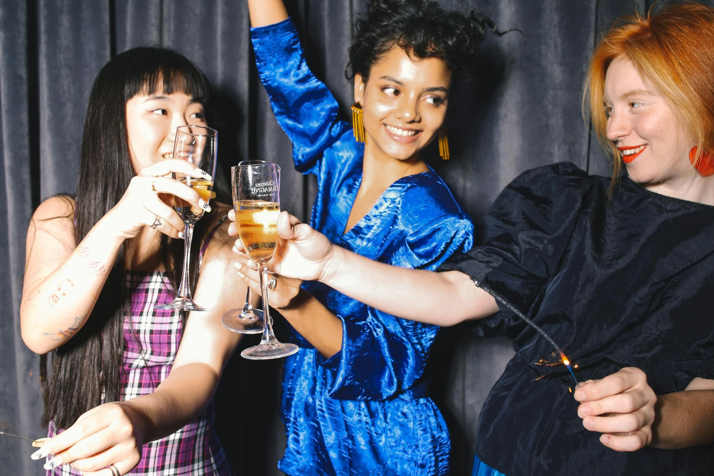 Group of people celebrating, holding glasses of champagne, in front of a dark curtains backdrop.