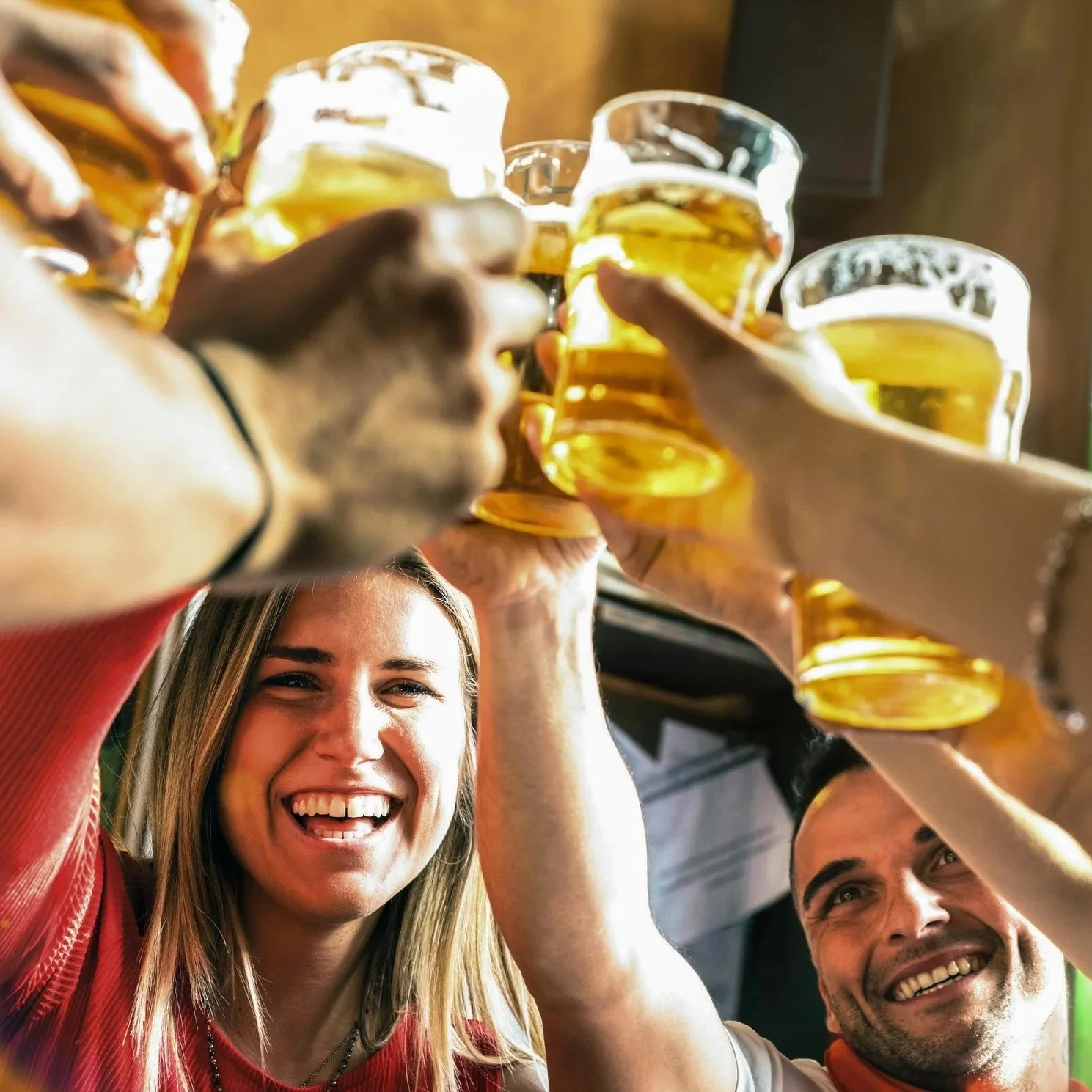 Group of friends raising glasses filled with beer in a toast, smiling and enjoying a celebration.