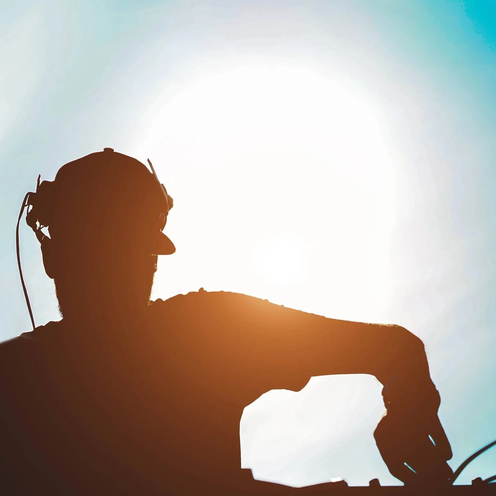 Silhouette of a person wearing flight helmet gazing upward against the sunlit sky.