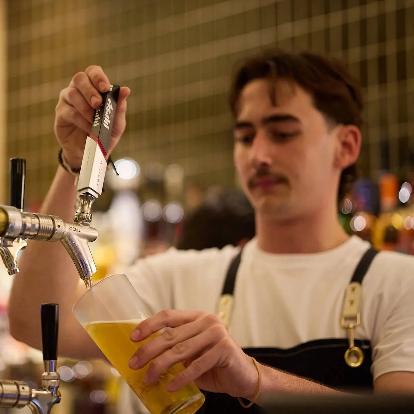 A young man pours a beer from a tap into a glass at a bar or pub.