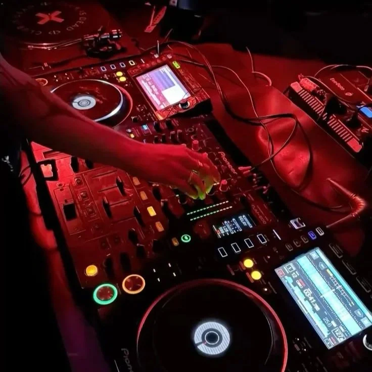 A DJ setup with turntables and a laptop at a party or club, with people dancing in the background.