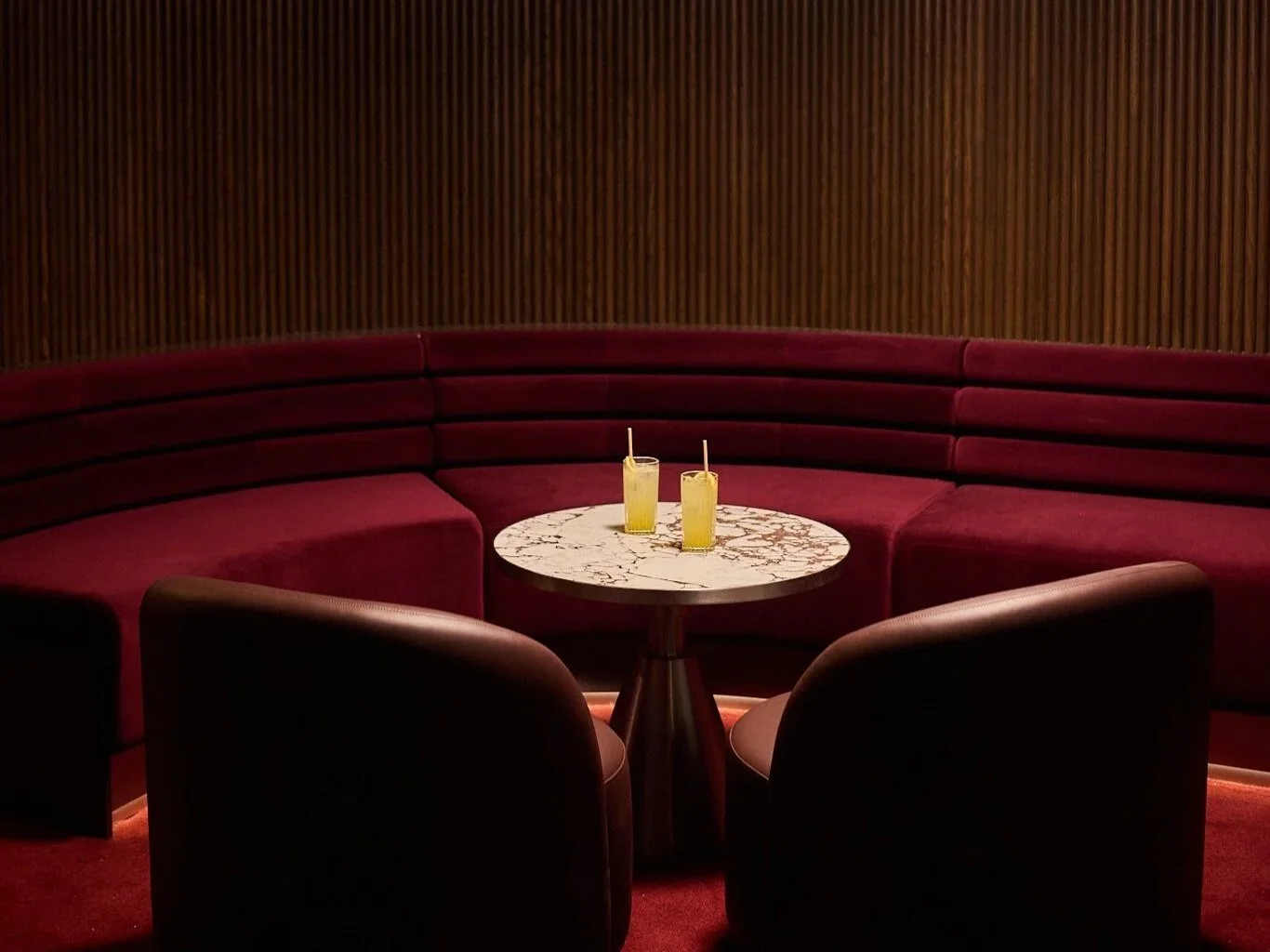 A cozy corner of Vixen Room, a round marble-top table, and two cocktails with straws.