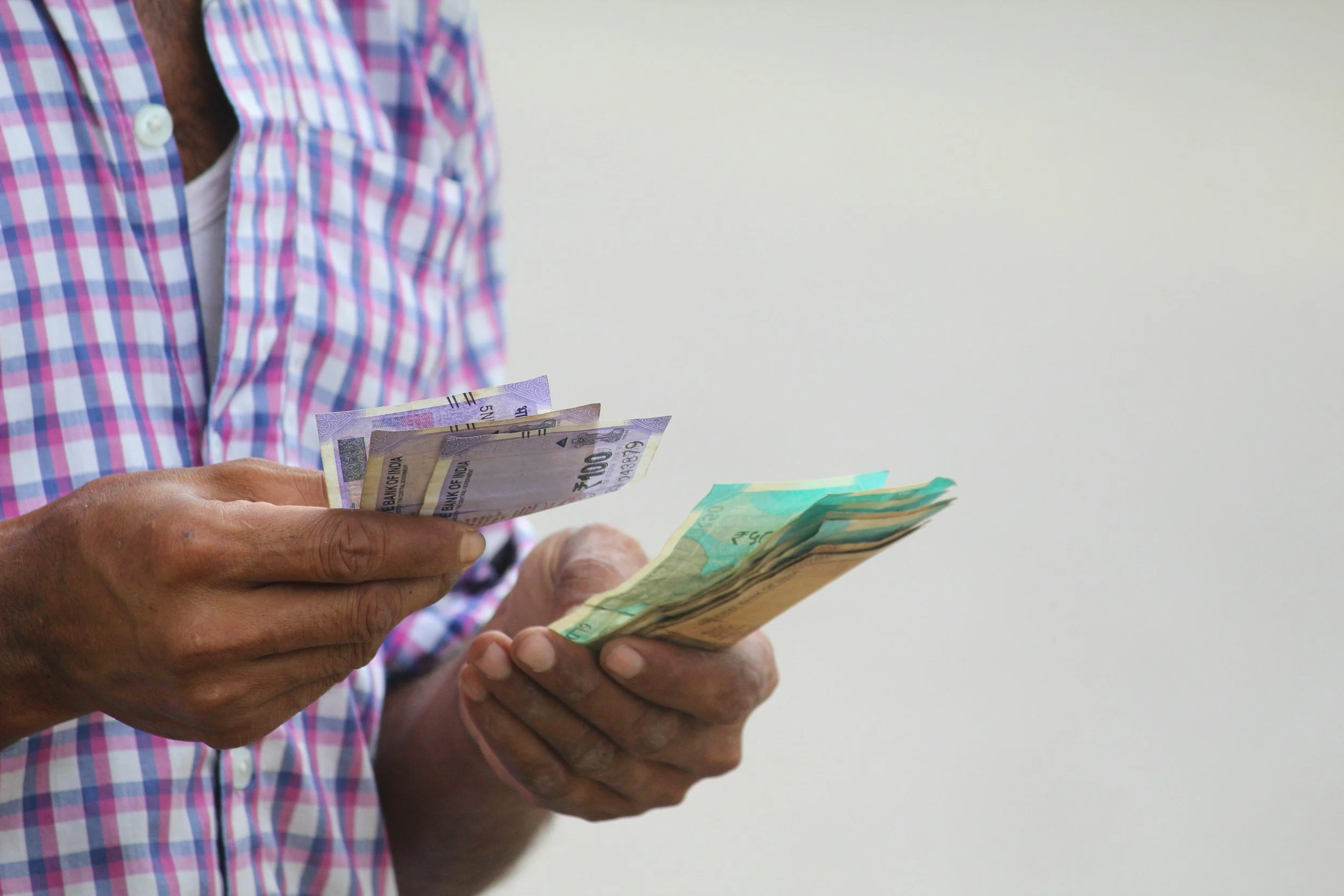 Person wearing a plaid shirt counting Indian currency notes.