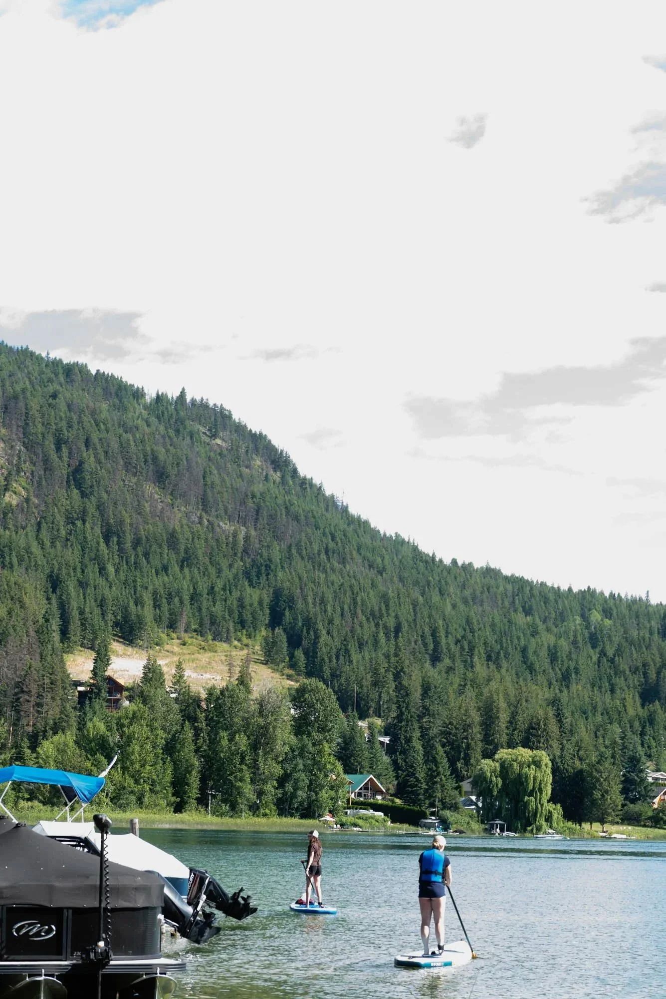 People paddleboarding, kayaking, and enjoying outdoor activities by a lake with a forested mountain in the background.