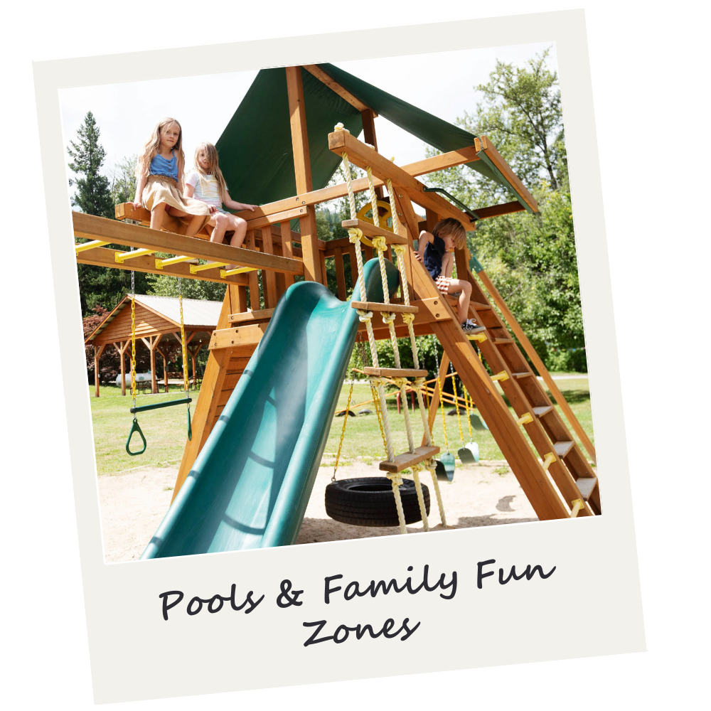 Children playing on a wooden playground structure with a slide and swings outdoors, surrounded by trees.