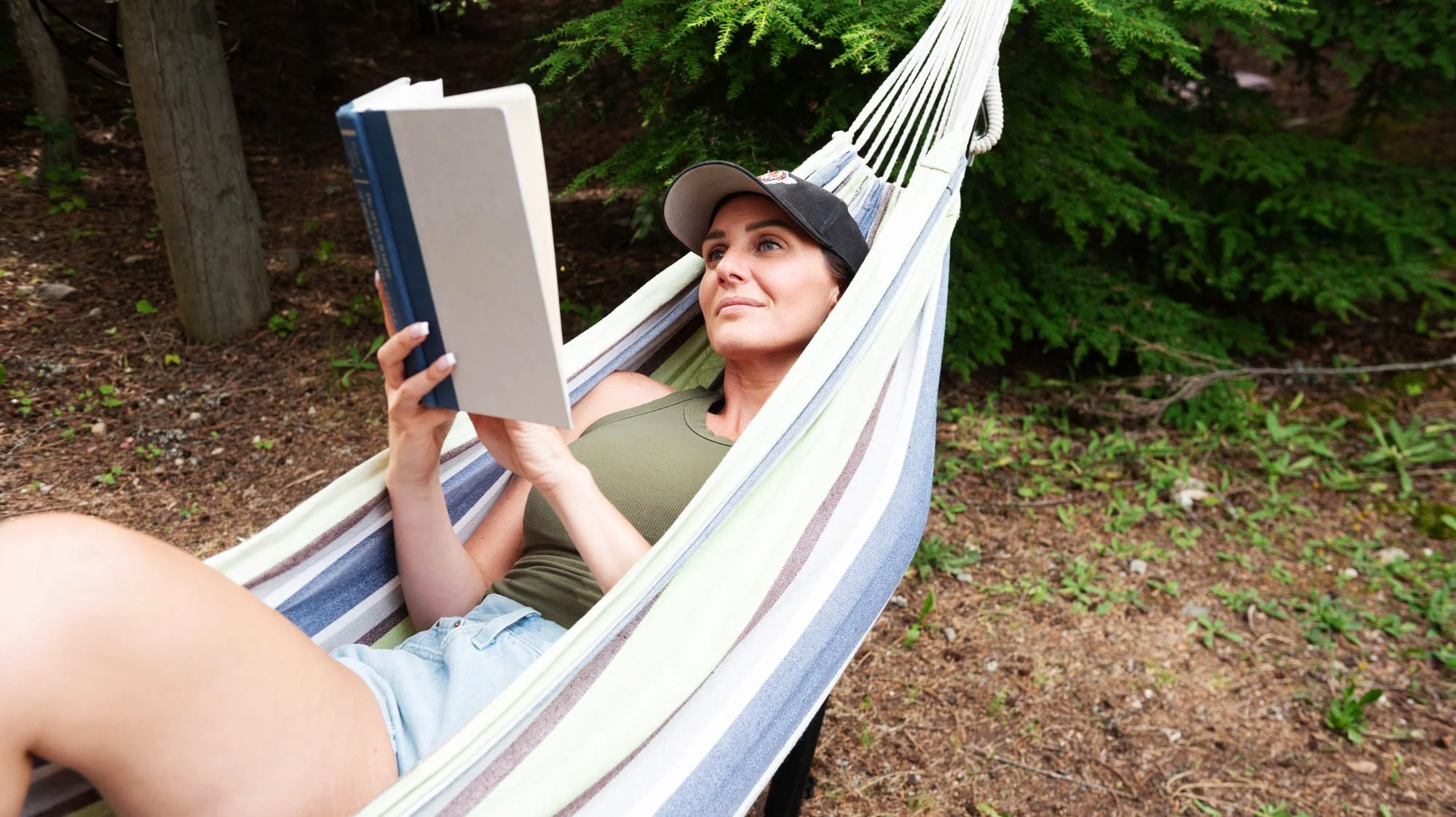 Woman relaxing in a hammock outdoors reading a book.