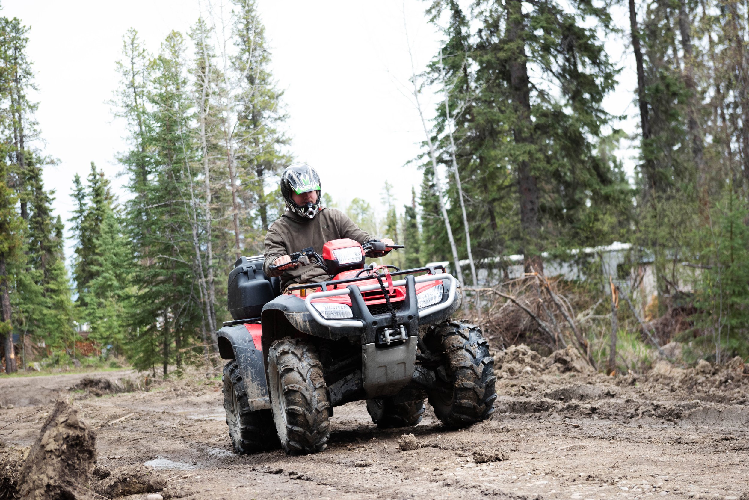 Person riding a red all-terrain vehicle (ATV) through a dirt trail surrounded by tall green trees.