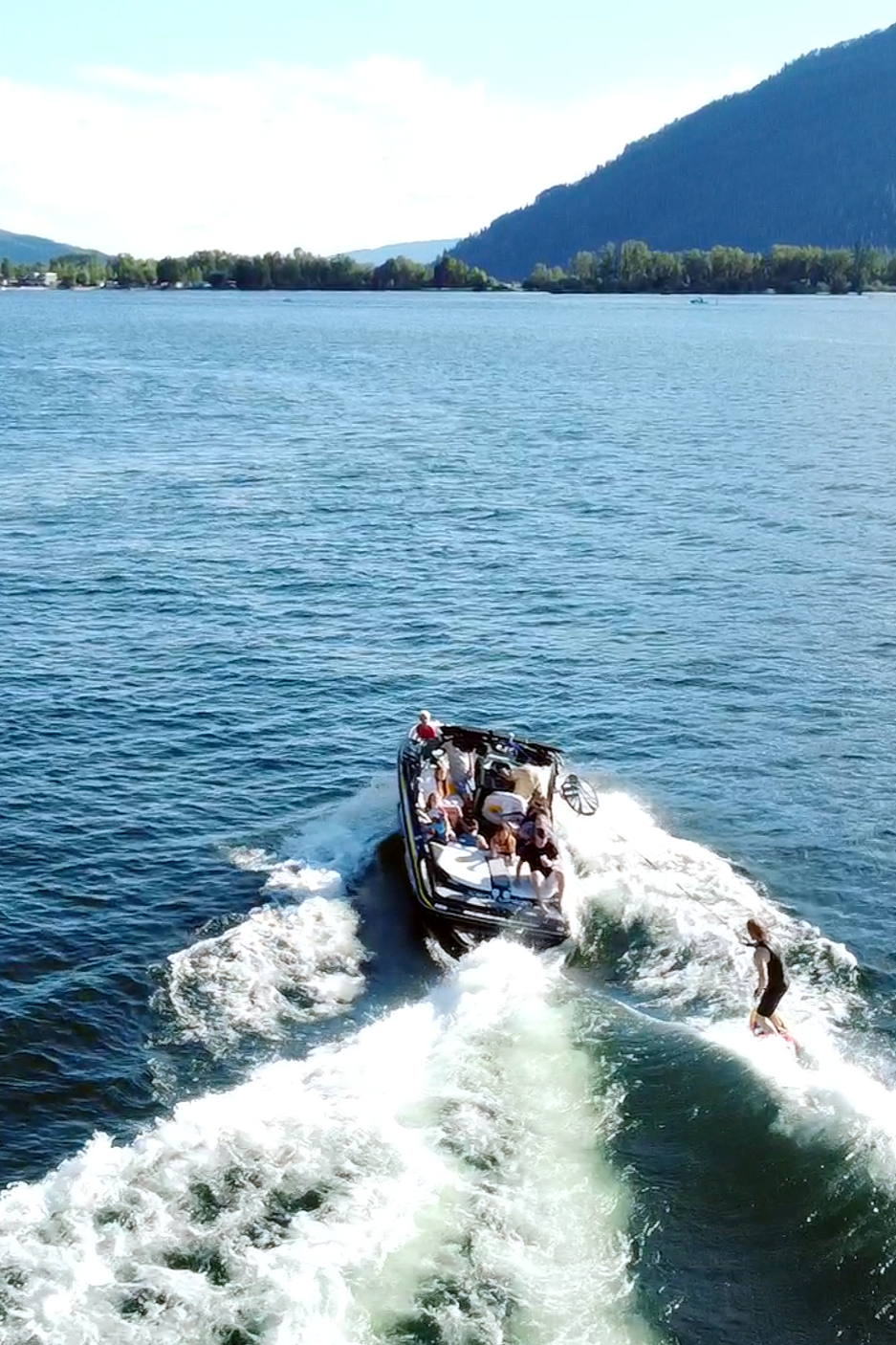 People enjoying a boat ride on a lake with mountains and trees in the background.