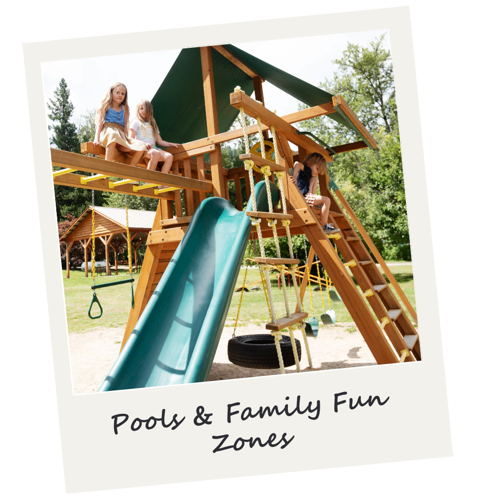 Children playing on a wooden playground structure with a slide and swings outdoors, surrounded by trees.