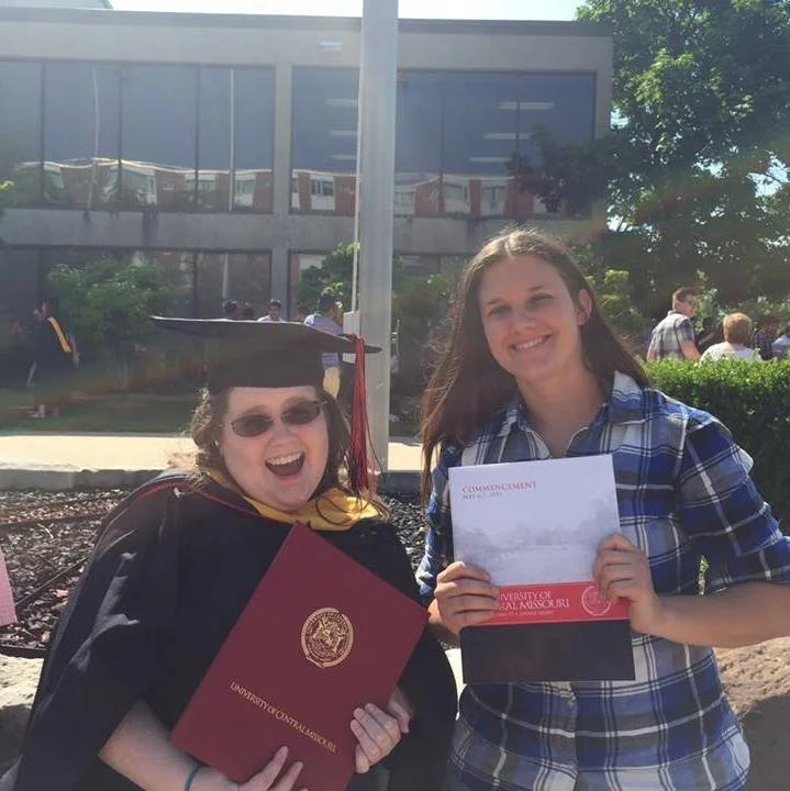 Happy young woman and graduate girl with diploma outdoors on sunny day, in front of a modern building.