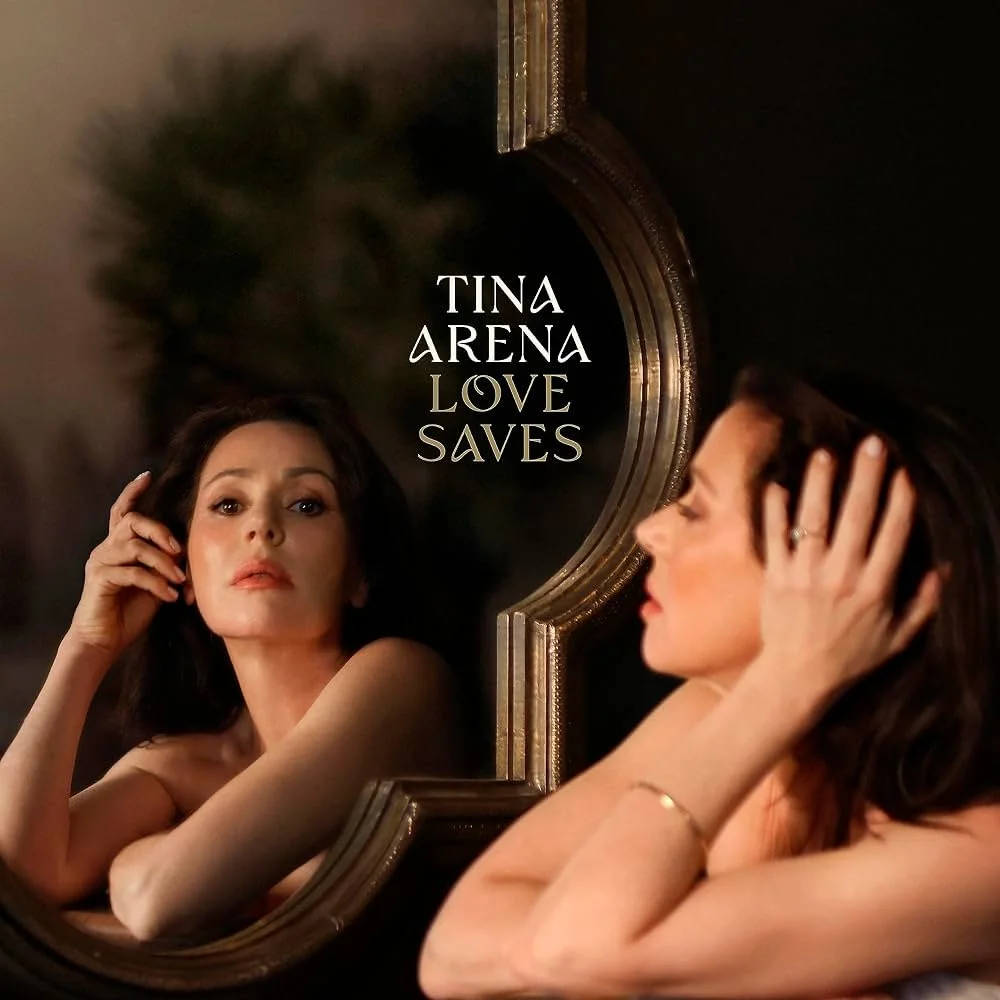 A woman looking into a mirror with the title 'Tina Arena Love Saves' overlaid, featuring her reflection and a blurred background.