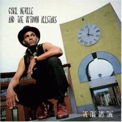 Album cover of girl with short hair, wearing black shirt and brown boots, sitting on a chair with a large clock and circular contraption behind her, with the text 'Girl with the Golden Apples' and 'The Fire in the Wind'.