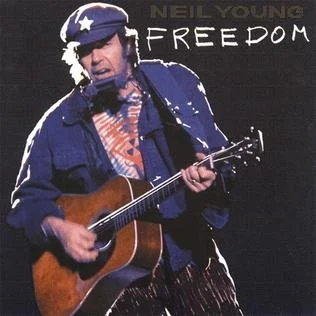 Neil Young wearing a star-spangled hat playing an acoustic guitar, with the word 'FREEDOM' written above him.