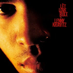 Close-up of a person's face with a nose ring, dark background, red text reading 'Let Love Rule' and 'Lenny Kravitz'.