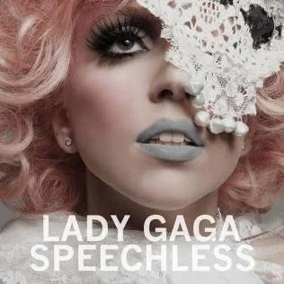 Close-up of Lady Gaga with pink curly hair, makeup, and lace detail over part of her face, with text 'Lady Gaga Speechless' at the bottom.