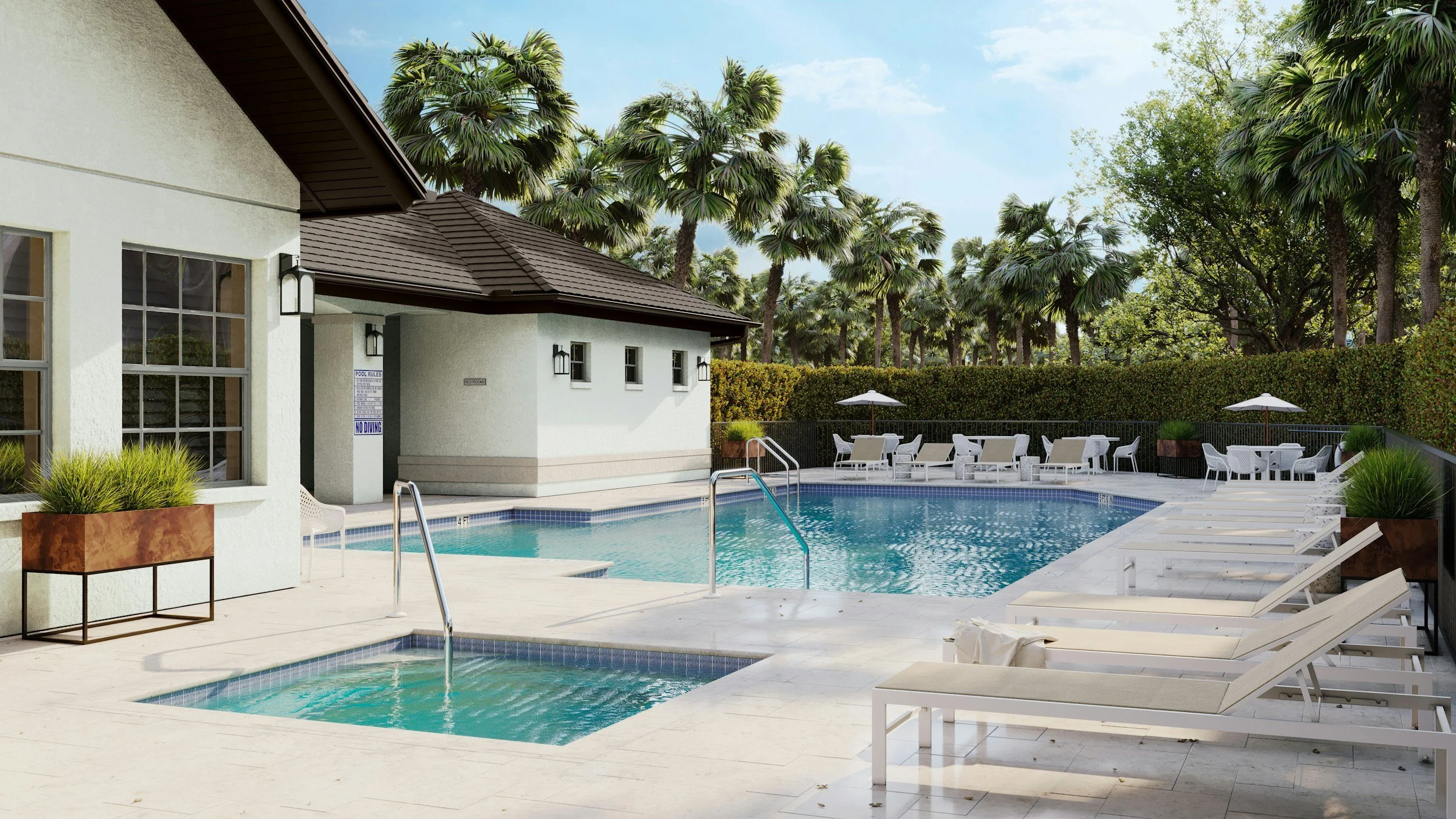An outdoor swimming pool area with lounge chairs, umbrellas, and a small hot tub, surrounded by palm trees and a white building with large windows.