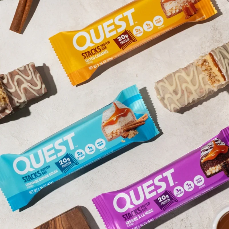 Three Quest protein bar packages in yellow, blue, and purple, arranged on a white surface.