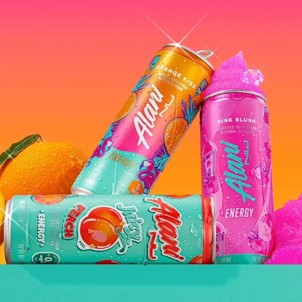 Three colorful cans of energy drinks from Alani Nu. A sliced orange and whole orange are in the background.