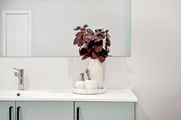 Bathroom sink and vanity with a potted plant in a white vase and a mirror above.