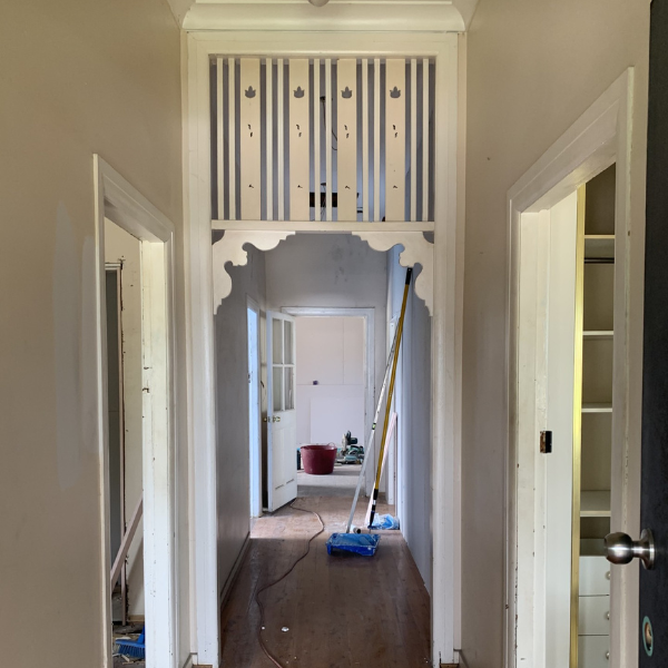View of a hallway with a decorative archway leading to another room, with a cleaning mop leaning against the wall, and open doors on both sides.