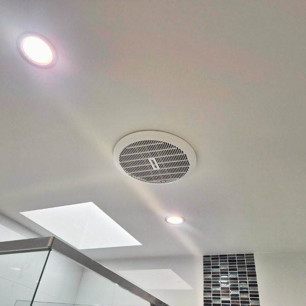 Ceiling with a central air vent, two recessed lights, a skylight, and a partially visible tiled wall.