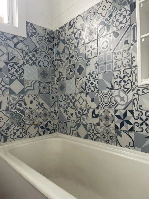 Bathroom corner with patterned blue and white ceramic tiles on the wall and white bathtub.