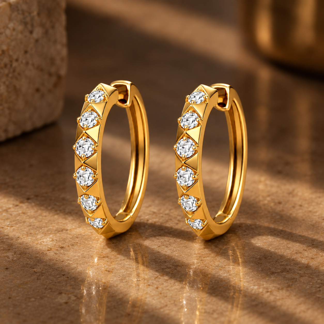 The Pyramid Diamond hoop earrings with embedded clear gemstones on a brown surface with shadow set in 18K Gold