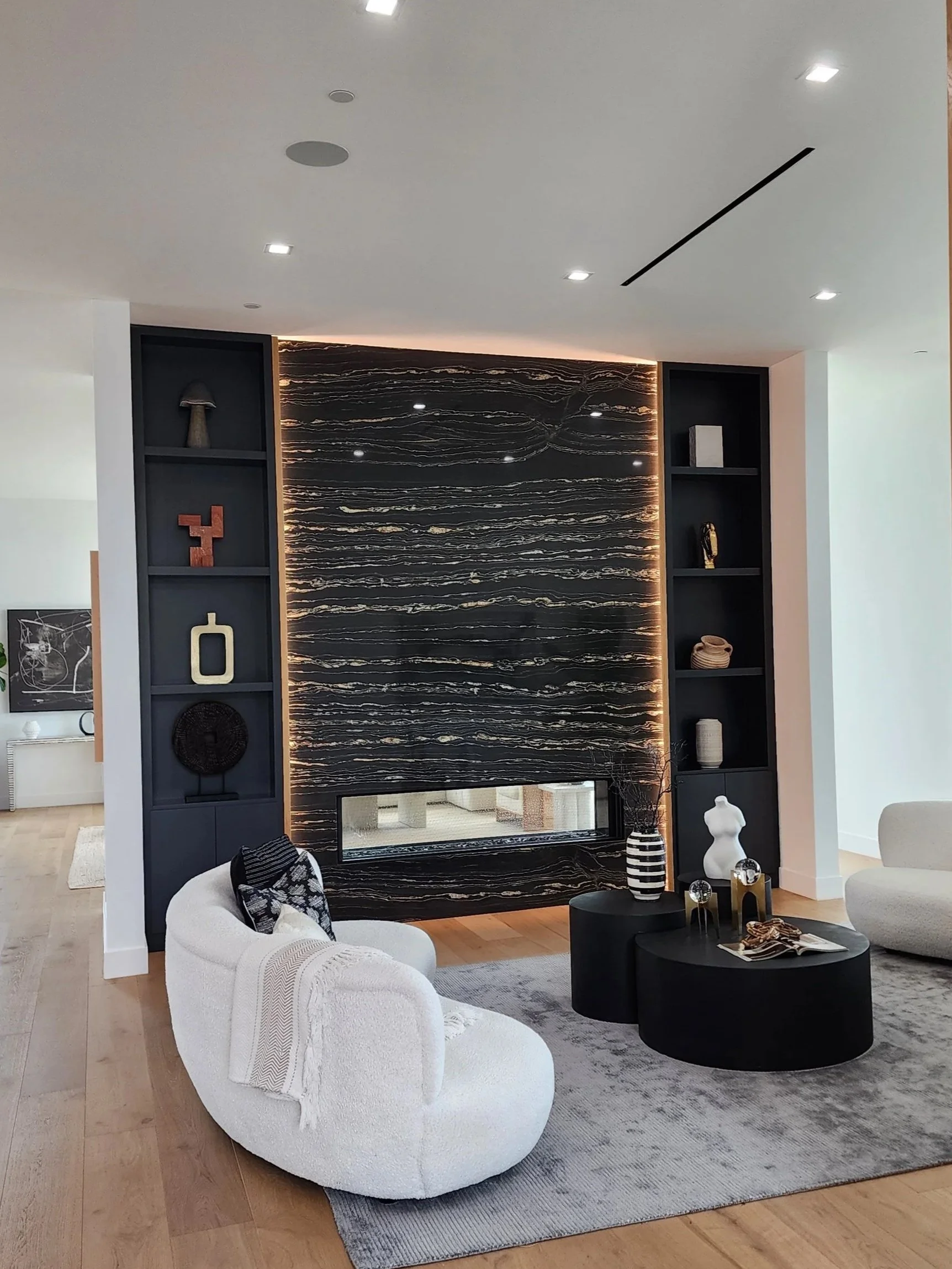 Modern living room with white and black furniture, a black marble fireplace, decorative objects, and a textured gray area rug.