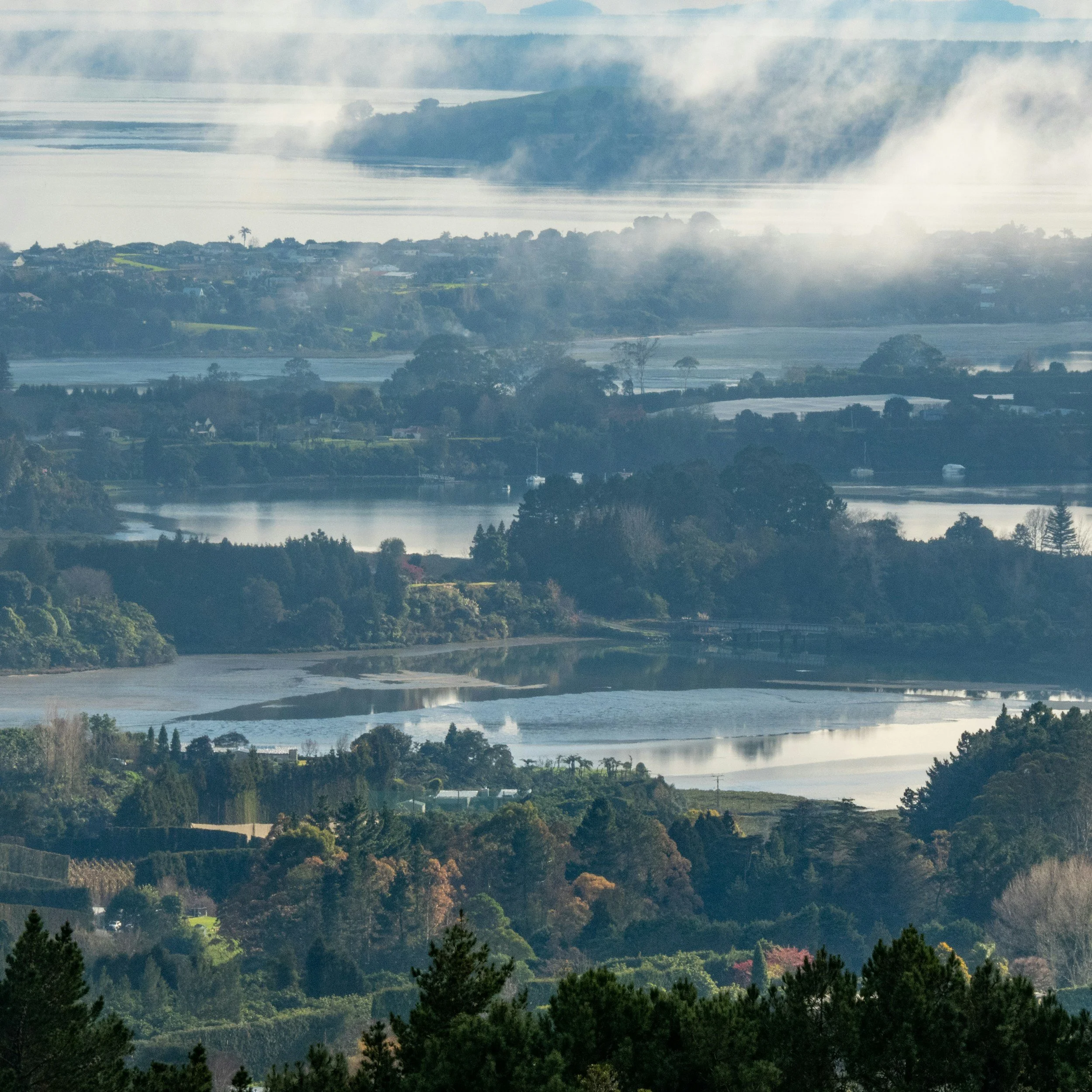 Scenic view of a river with hills, trees, and houses in the distance under a cloudy sky.