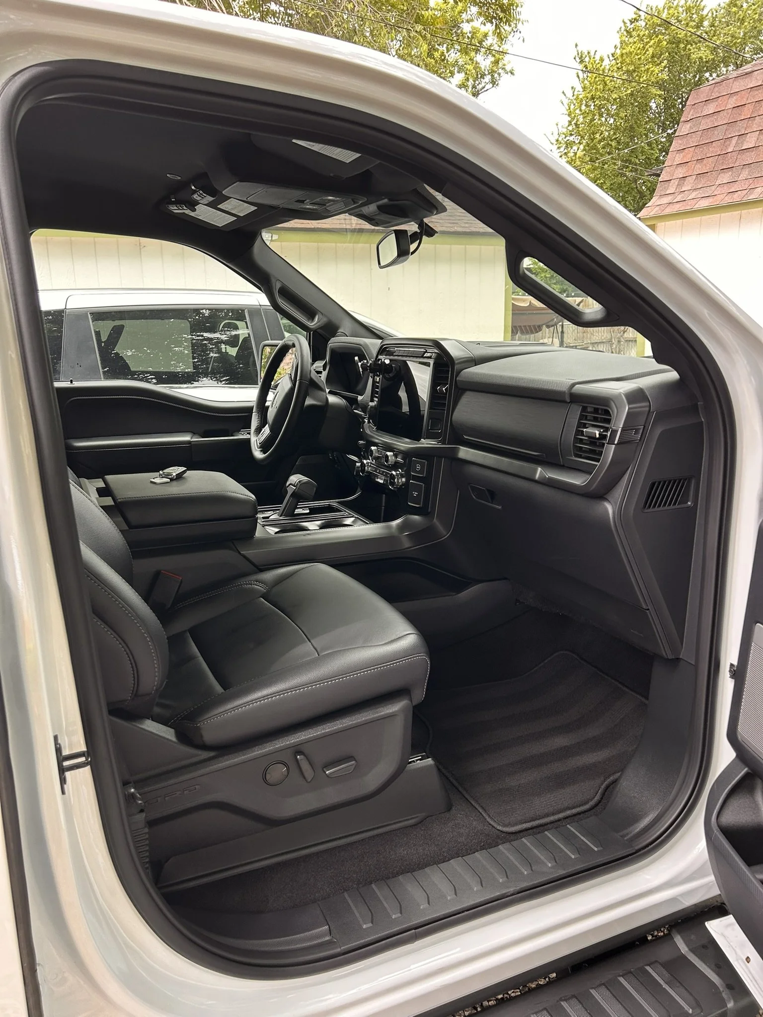 The interior of a modern vehicle, showing the driver's seat, dashboard, steering wheel, and center console, with an outdoor view through the windows.