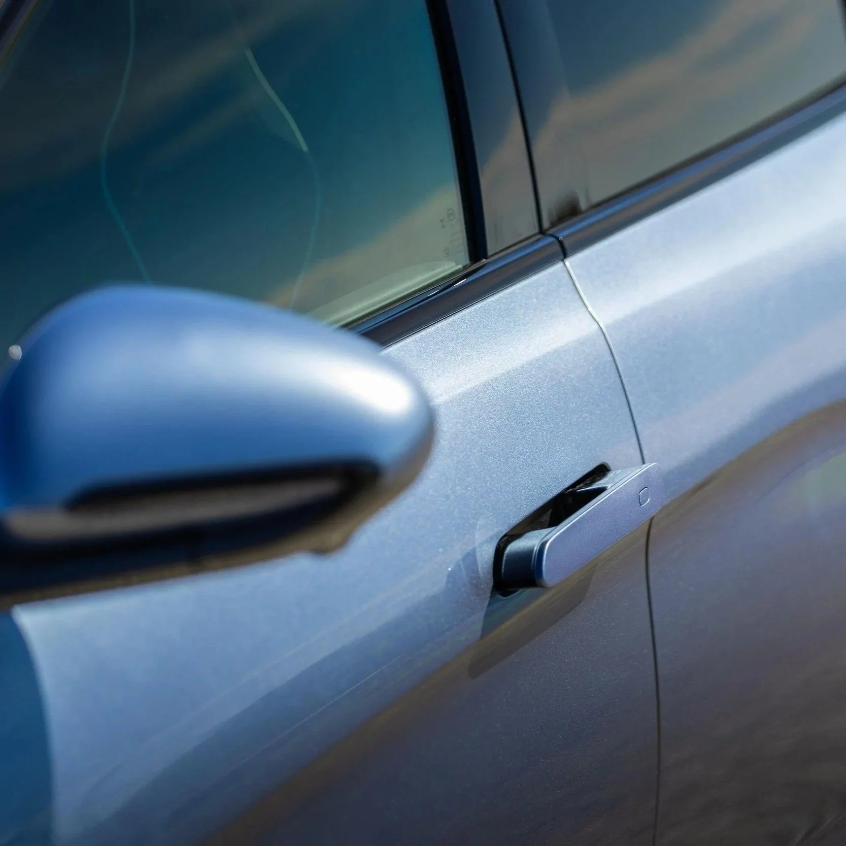Close-up of a metallic blue car door, showing the side mirror, window, and body panel.