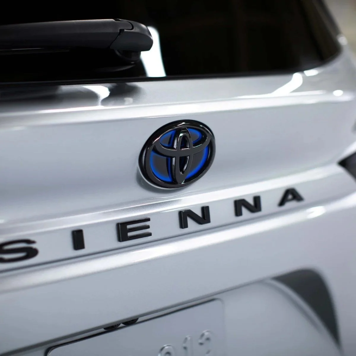 Close-up of the rear of a silver Toyota SiENNA with the Toyota logo illuminated in blue on the trunk.